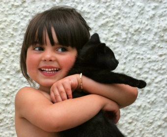Cliona Schuurman-Smith aged three, holding an all black kitten and smiling.